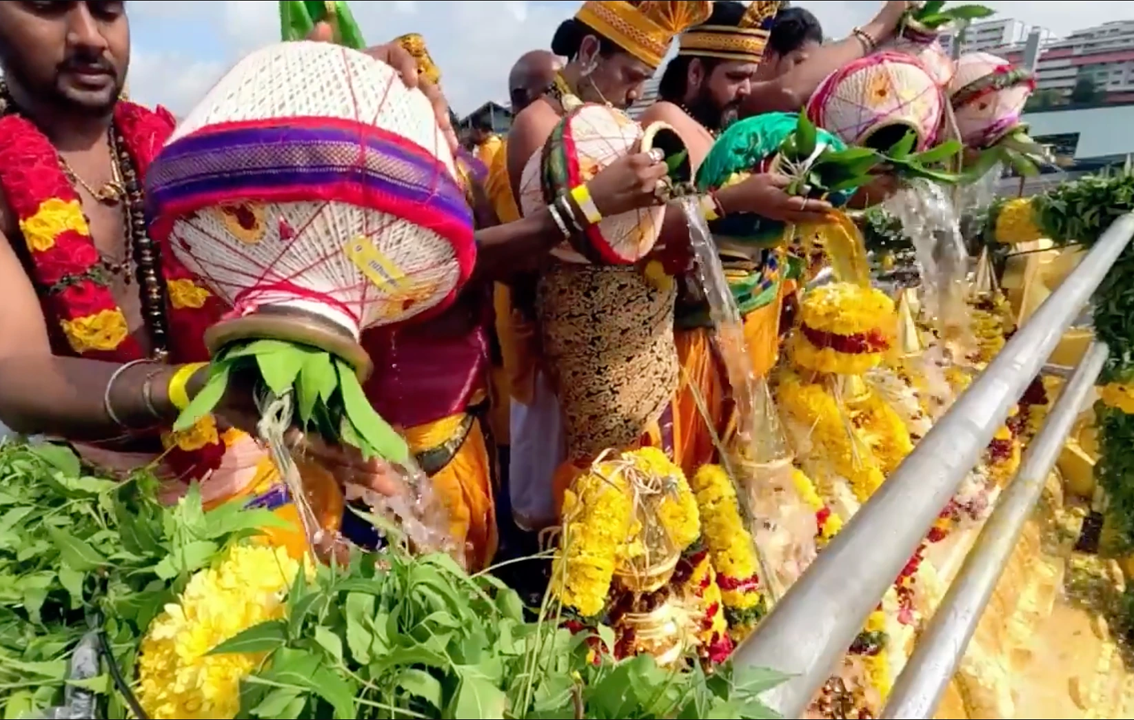 Priests pour sacred water from decorated kalasam pots over marigold-garlanded kalasams during the Maha Kumbhabishegam at Sree Maha Mariamman Temple, Singapore